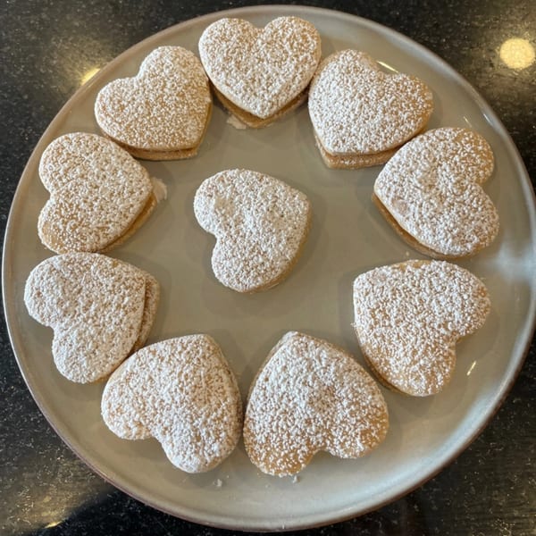 A plate of heart-shaped Peruvian alfajores, dusted with powdered sugar, arranged in a circle.