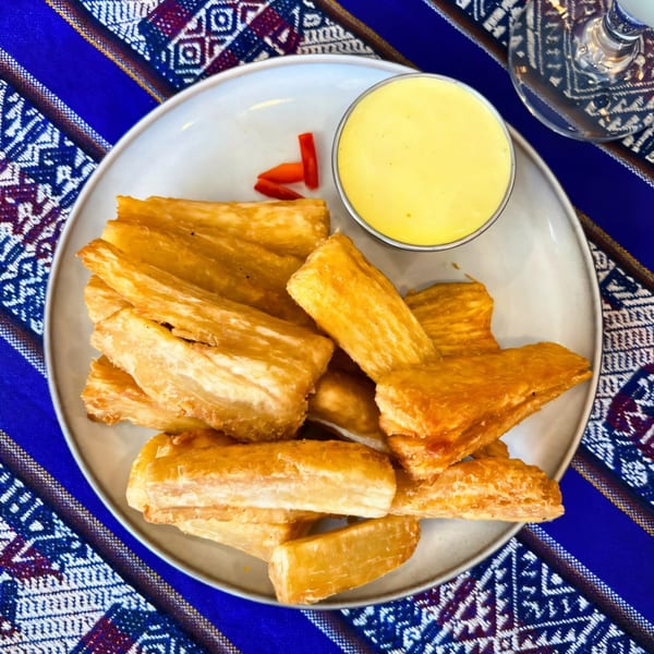Fried yuca sticks with a side of yellow huancaina sauce and red chili peppers on a plate.