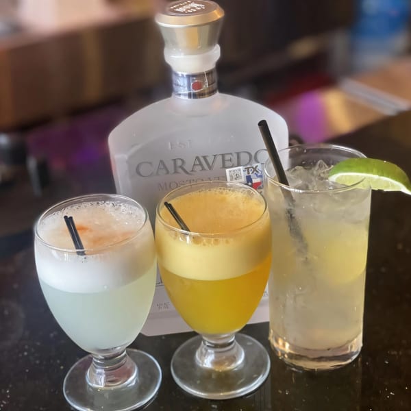 Three Peruvian cocktails, including Pisco Sours, with a bottle of Caravedo Pisco in the background.