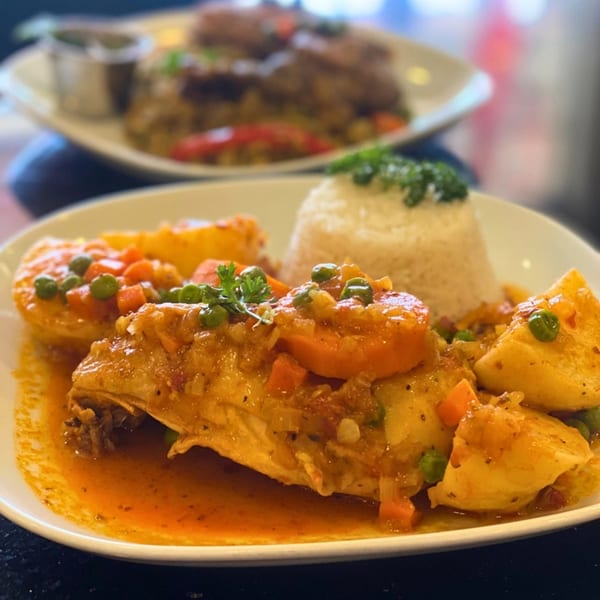 Peruvian chicken stew with potatoes, carrots, peas, and rice on a white plate.