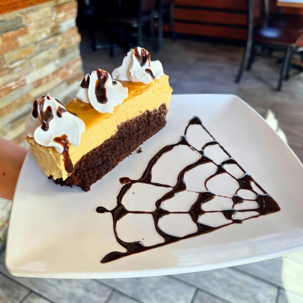 Slice of Peruvian passion fruit cheesecake with chocolate drizzle and whipped cream on a white plate.